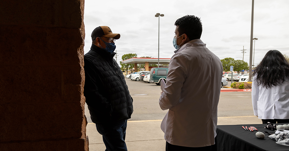 two men in masks talk outside of Amigos supermarket