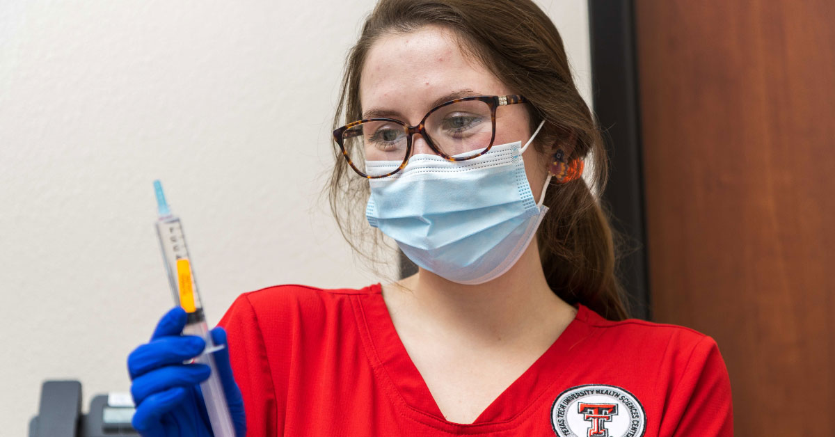 Nursing student wearing TTUHSC red scrubs and gloves.
