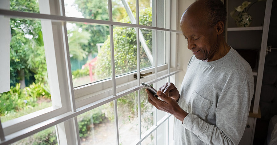 elderly man standing by a window with his phone