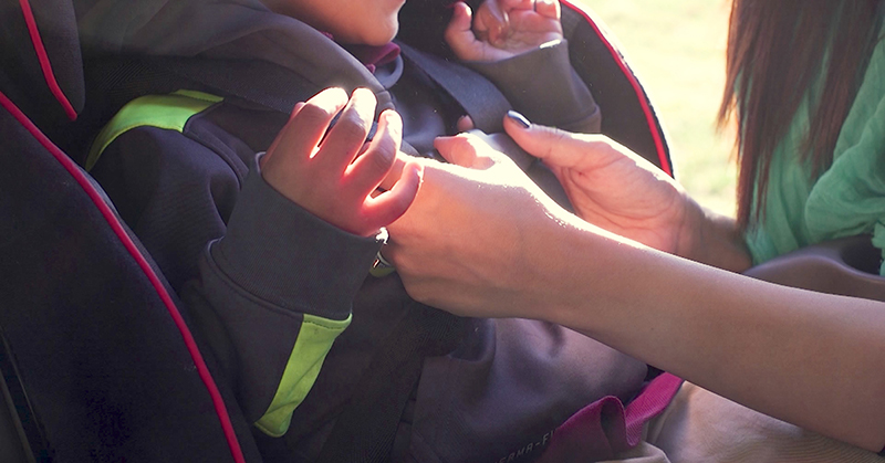 hands fastening a child into a car seat