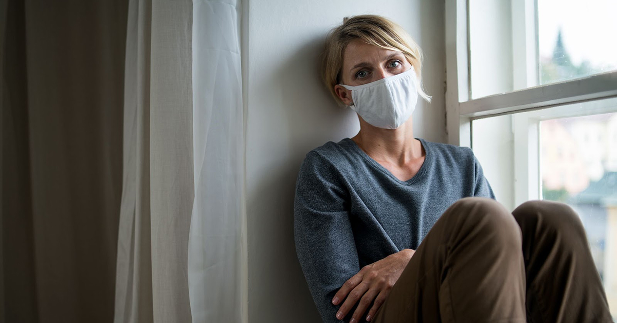 Woman wearing covid-19 mask sitting by a window