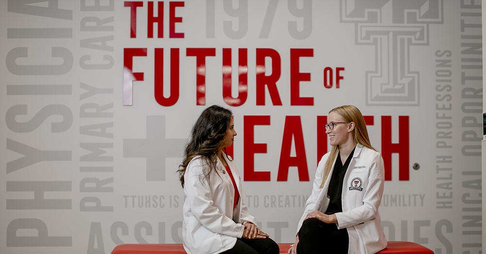 two health care professionals talking on a bench with "the future of health" written on the wall behind them