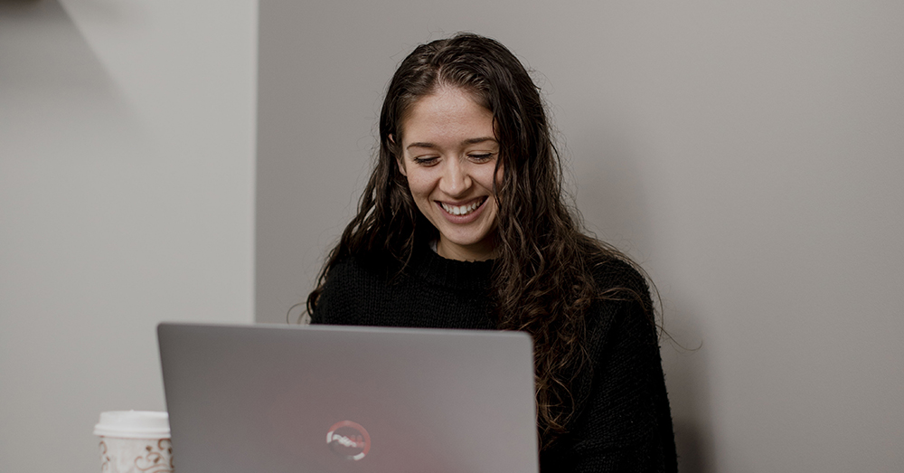 woman smiling at her laptop with coffee