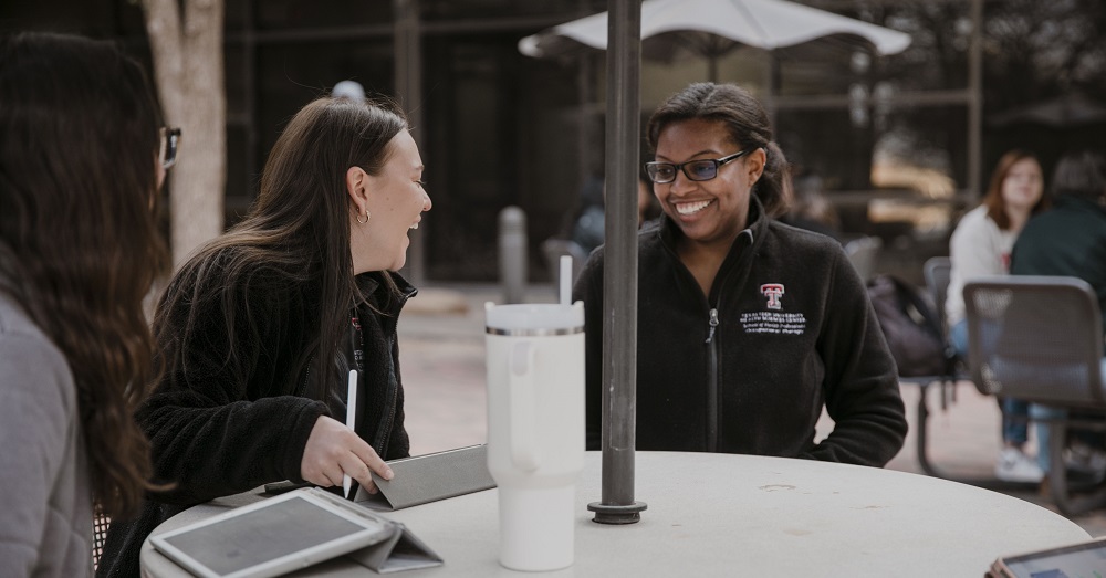 two students sitting at an outdoor table laughing together