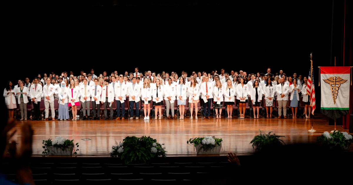181 TTUHSC medical students wear white coats and stand on a stage.