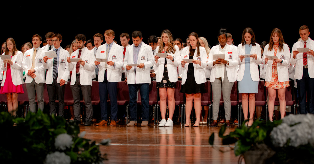 TTUHSC medical students wear white coats and stand on a stage.