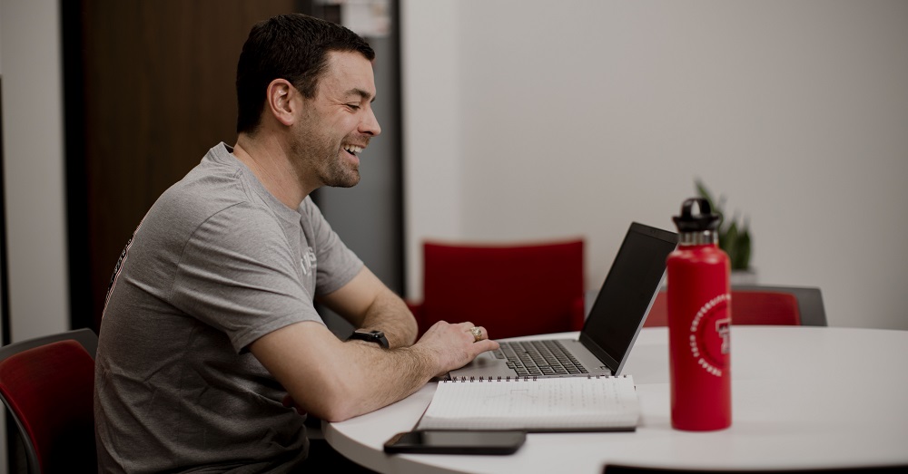 man sitting at table, working on his laptop