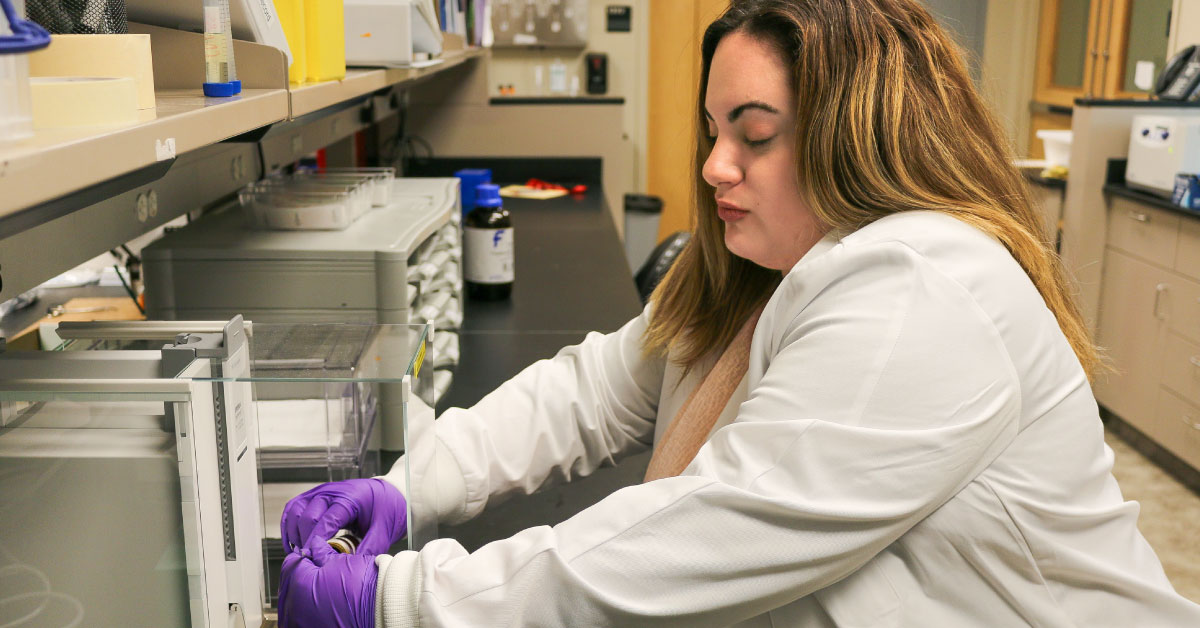 Female TTUHSC researcher wears a white coat and works in her lab.