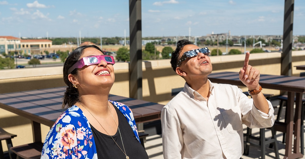 two people looking toward the sky wearing eclipse safety glasses