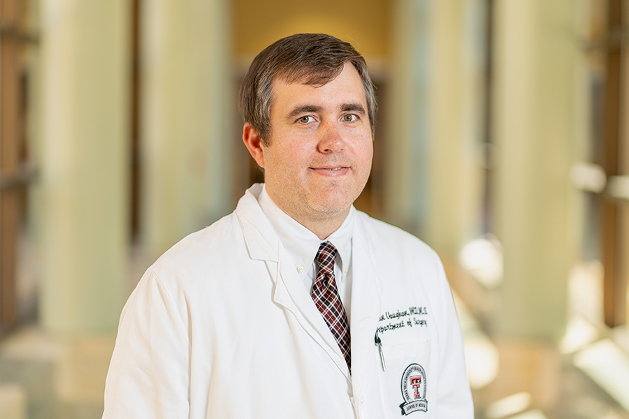 Male TTUHSC surgeon wears his white coat and stands in a hallway.