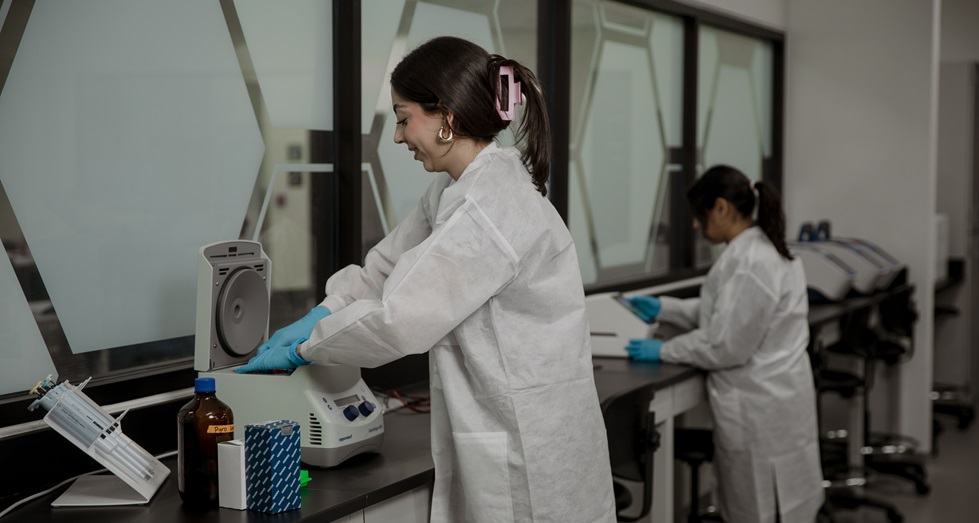 womann in scrubs and gloves working with DNA equipment in a lab
