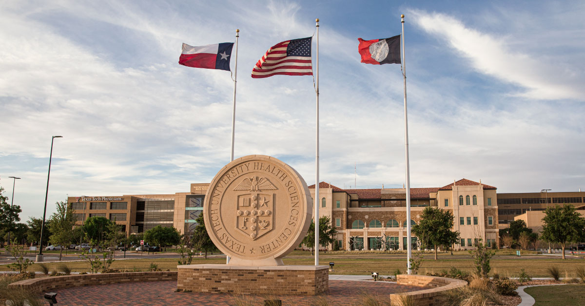 Large stone TTUHSC university seal outside of a campus building with flag poles behind it.