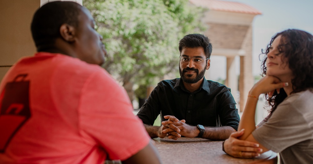 three students talking around a table