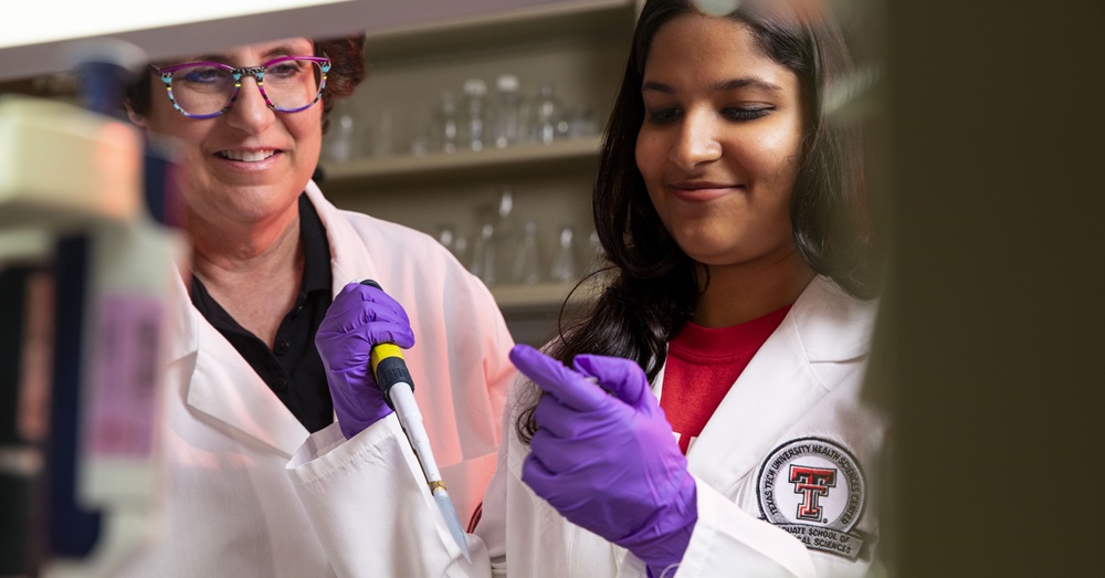 two women working in a lab with equipment, wearing whitecoats