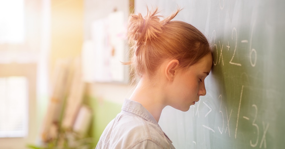 young woman resting her head against a chalkboard in fatigue