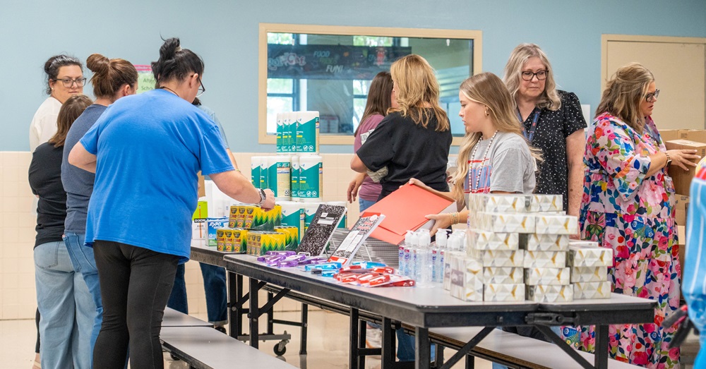 People indoors at a school set up school supplies on tables