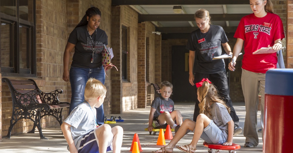 children playing on scooters while camp leaders watch