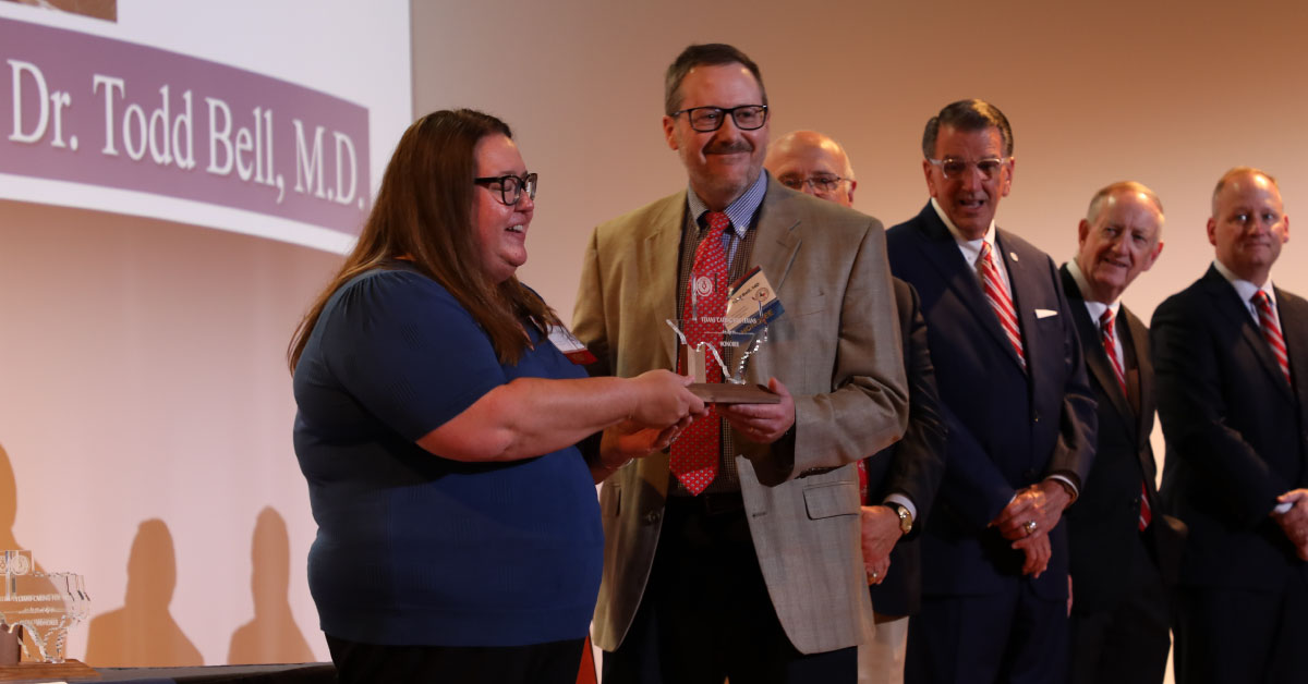 Male TTUHSC physician is handed a trophy from a woman while standing on stage.