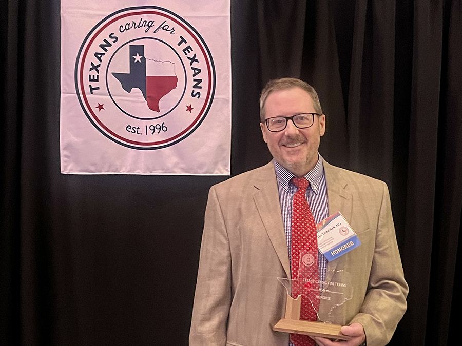 Male TTUHSC physician holds a trophy and stands under a banner that reads, "Texans Caring for Texans."