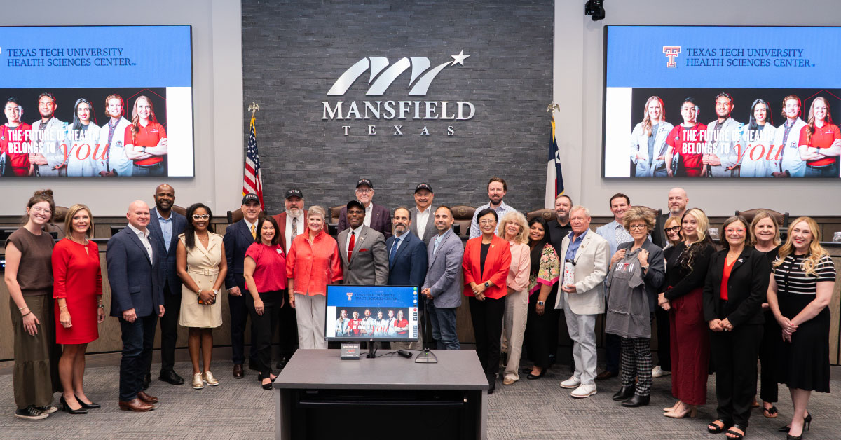 Large group of people stand beneth the City of Mansfield logo hanging on a wall.