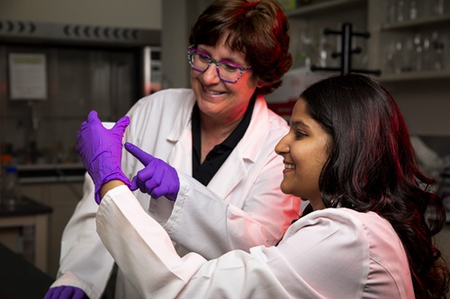 a student and teacher in lab coats look at a vial in a lab