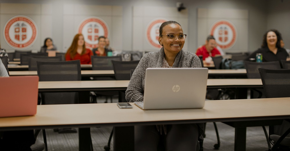 student smiling with laptop in a classroom