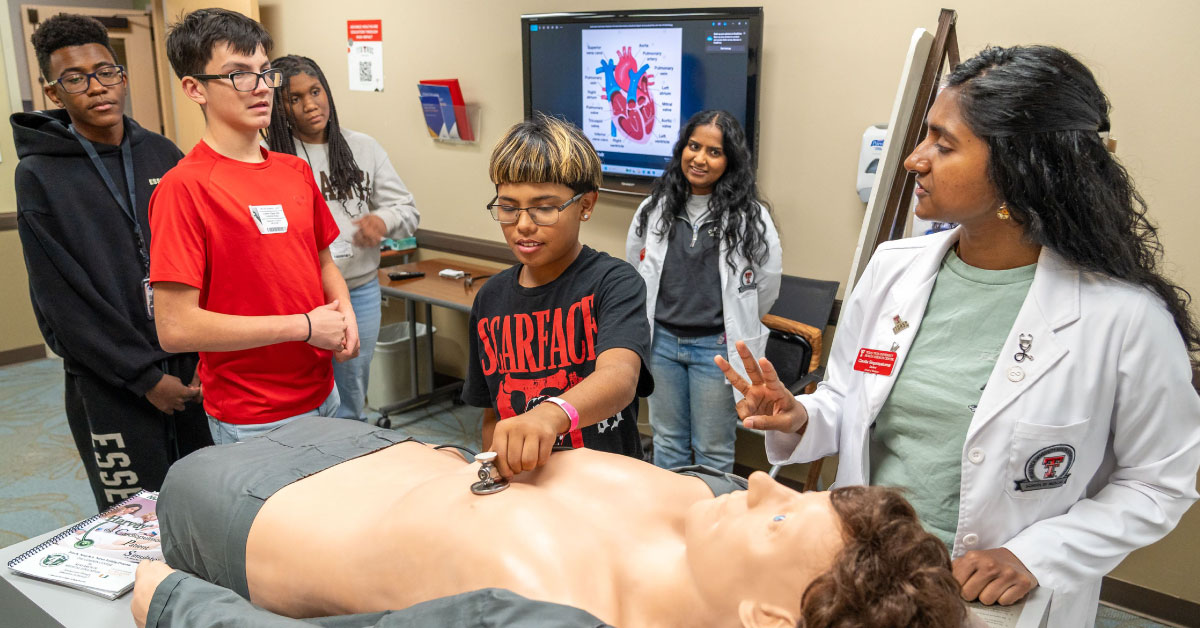 Female medical student teaches midle school students over a simulation manikin.