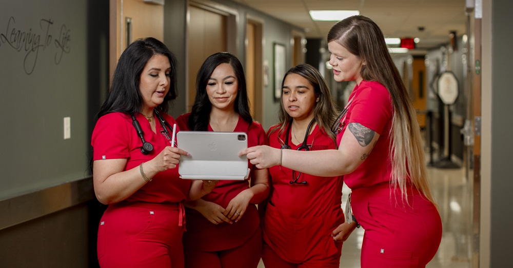 four nurses in red scrubs looking at an ipad