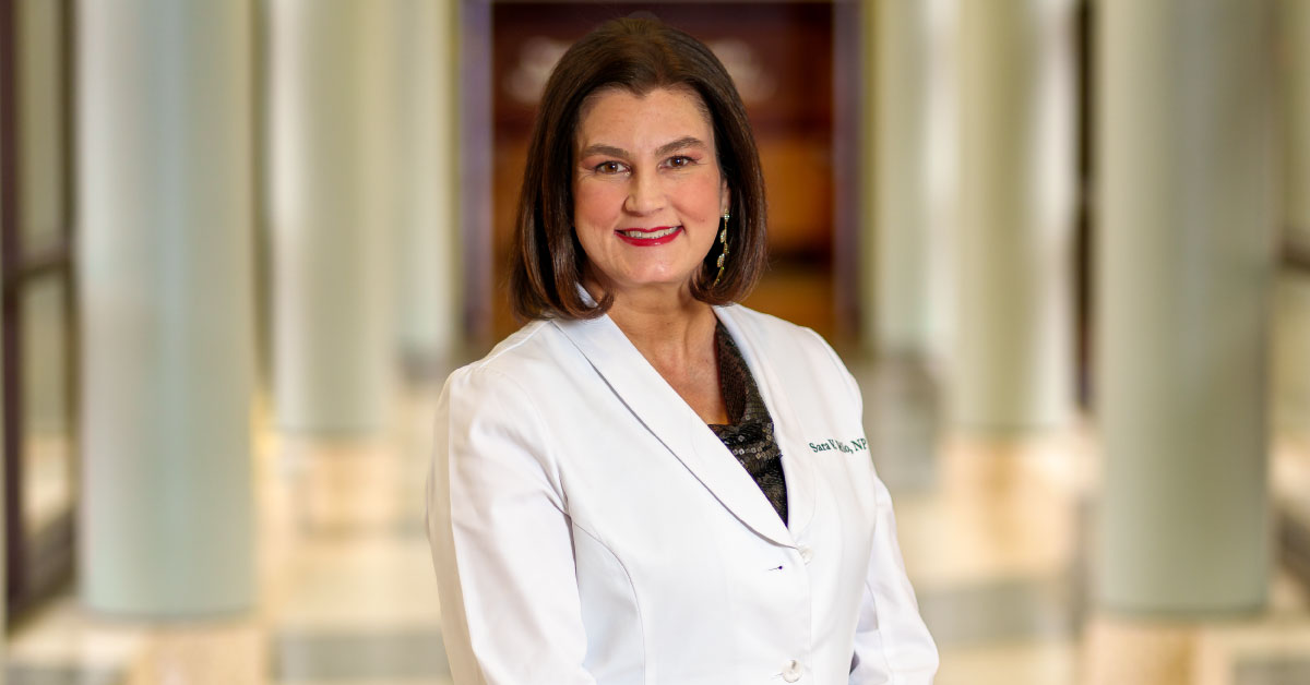 Woman nurse practitioner wears a white coat and stands in a hallway.