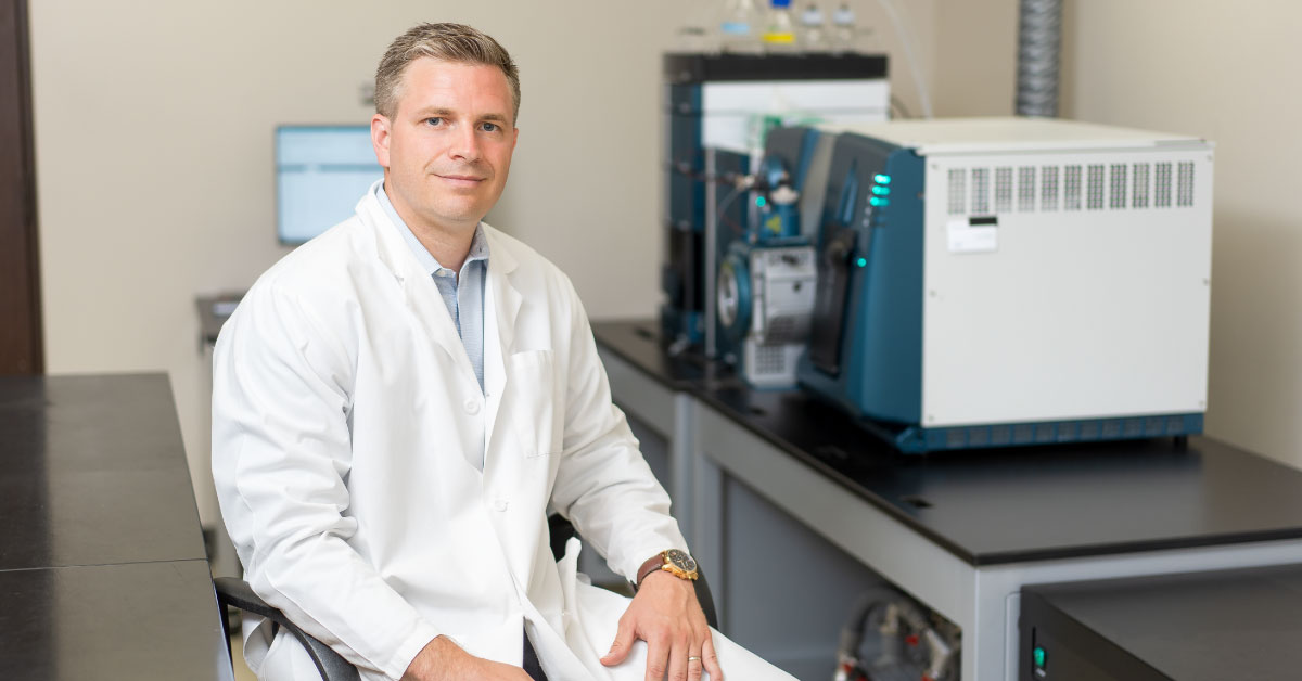 Male TTUHSC researcher wears a white coat and sits in his lab.