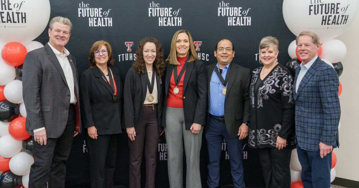 Seven people stand in front of a TTUHSC “Future of Health” photo backdrop.