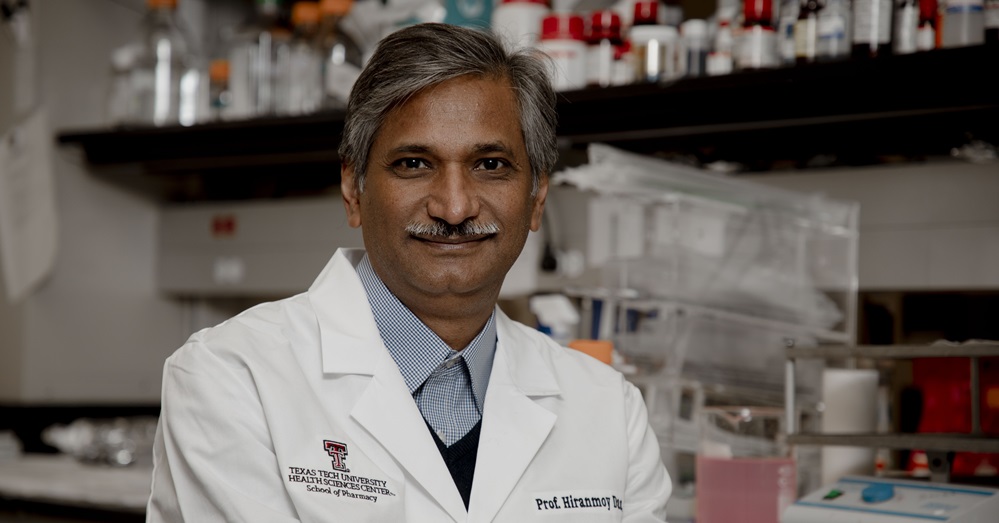 doctor in a white coat sitting in a lab, looking at the camera