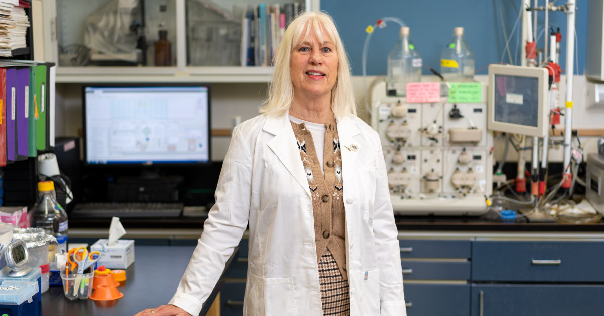 Woman researcher stands in her lab while wearing a white coat.