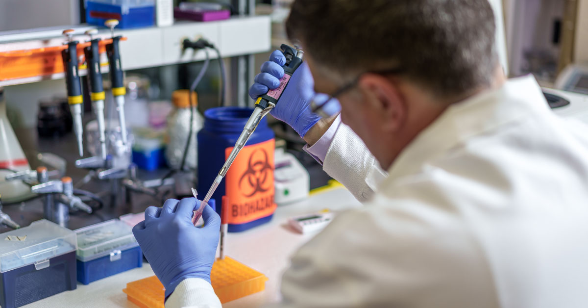 Man researcher wears white coat and blue gloves while working with vials in his lab.