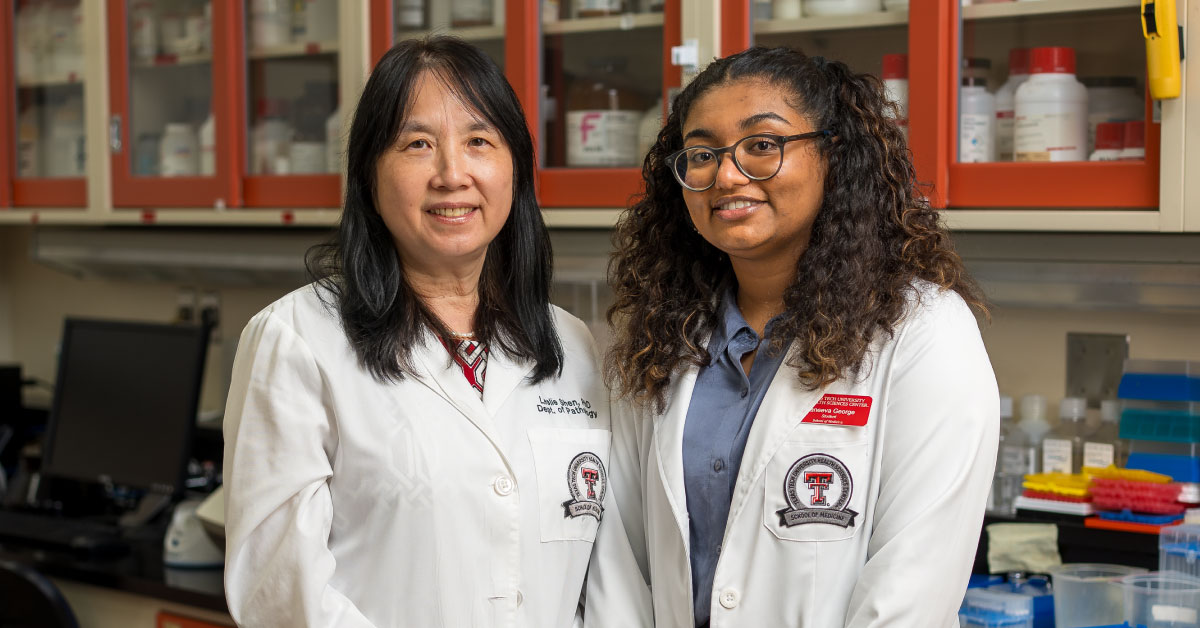 Two women stand together wearing white coats.