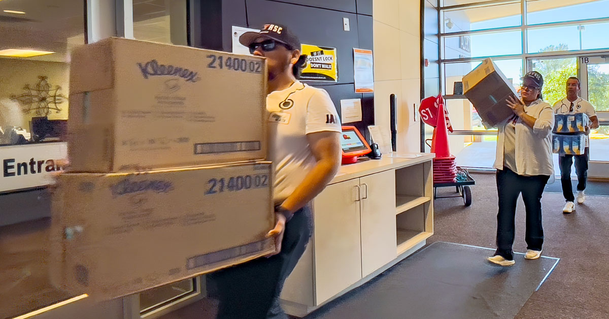 Three people carry boxes of school supplies into a school.