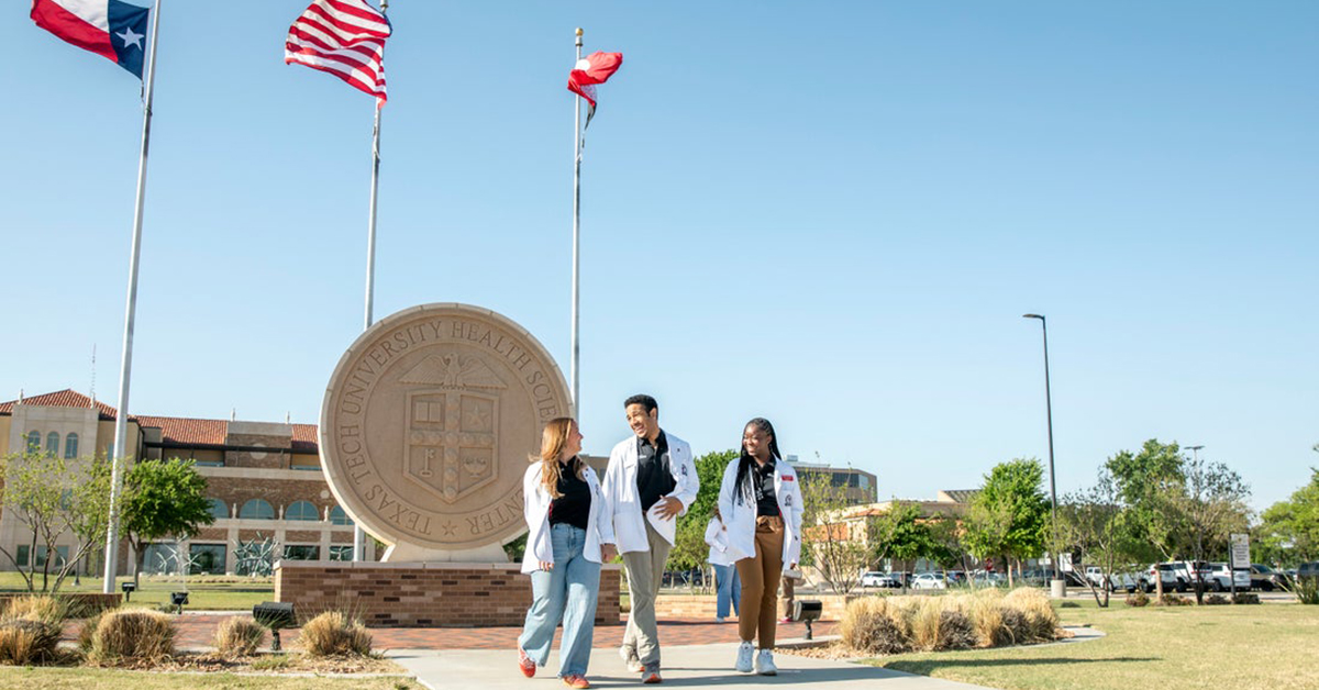 Several medical stuents walk outside in front of the TTUHSC university seal.