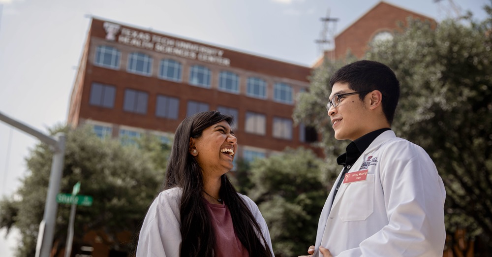 Two TTUHSC pharmacy professionals laughing outdoors in front of the Dallas campus 