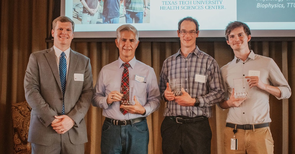 four men stand holding awards