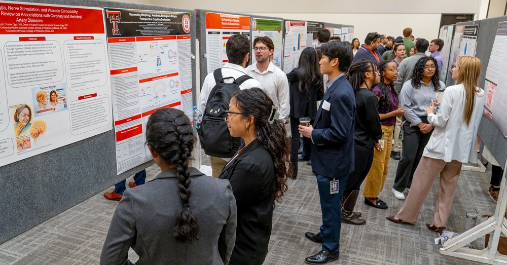 medical students stand in groups discussing their research poster presentations