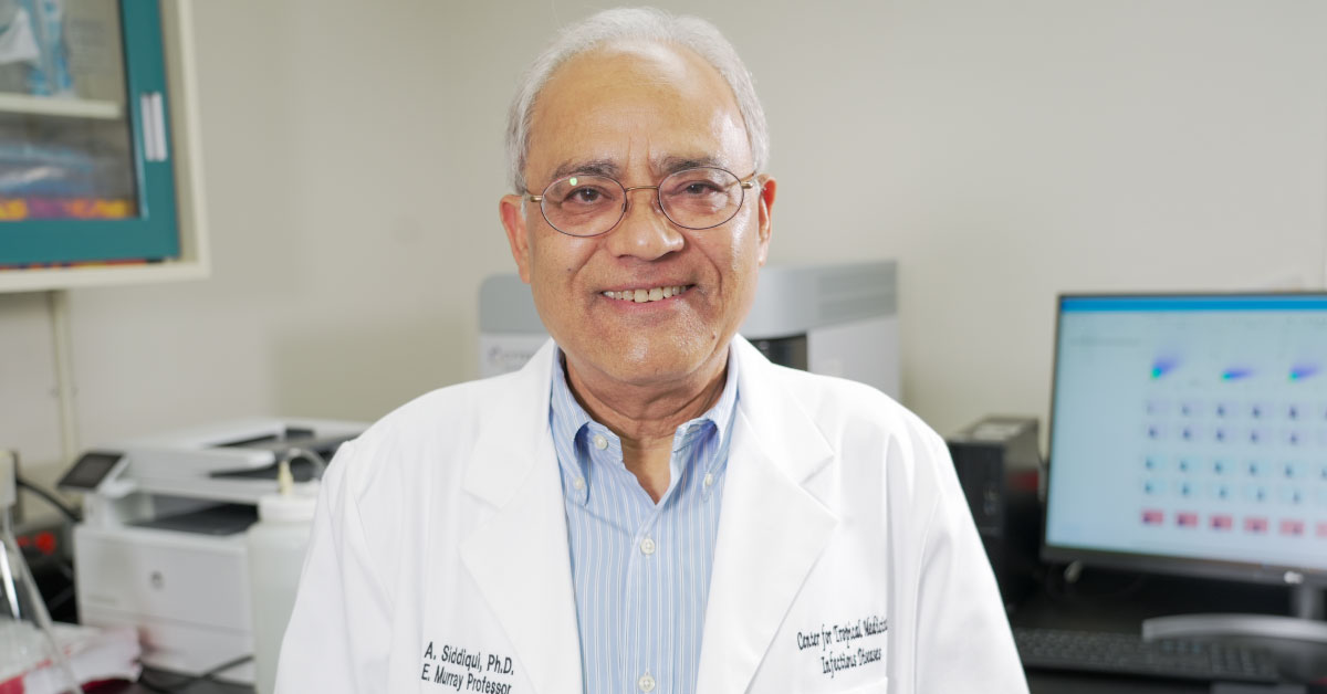 Afzal Siddiqui, Ph.D., wears a whit coat in his office with a computer in the background.