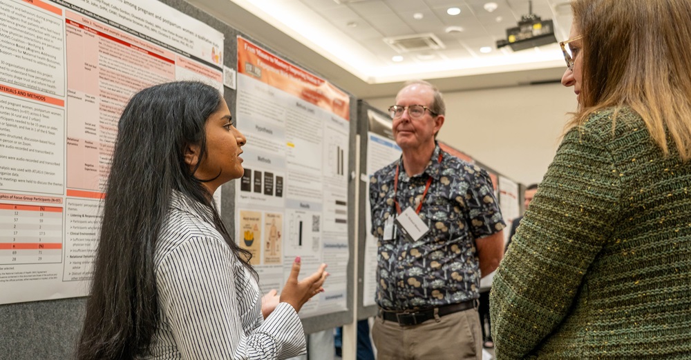 a student discusses her poster presentation with two listeners