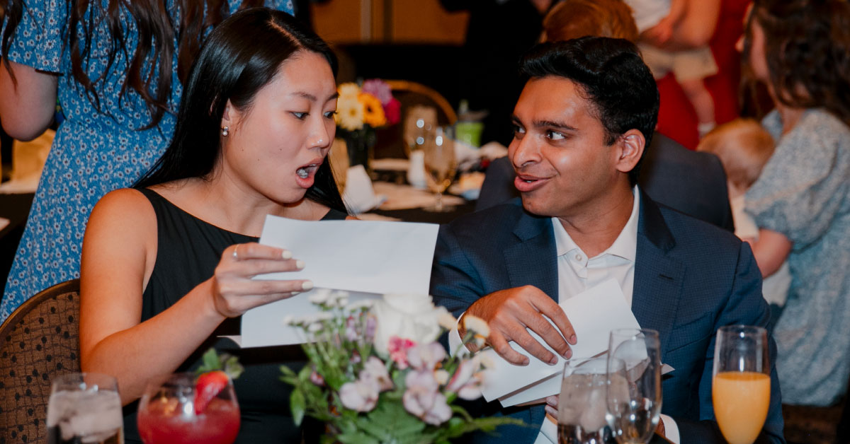 One man and one woman each open their match envelopes with surprised looks on their faces.