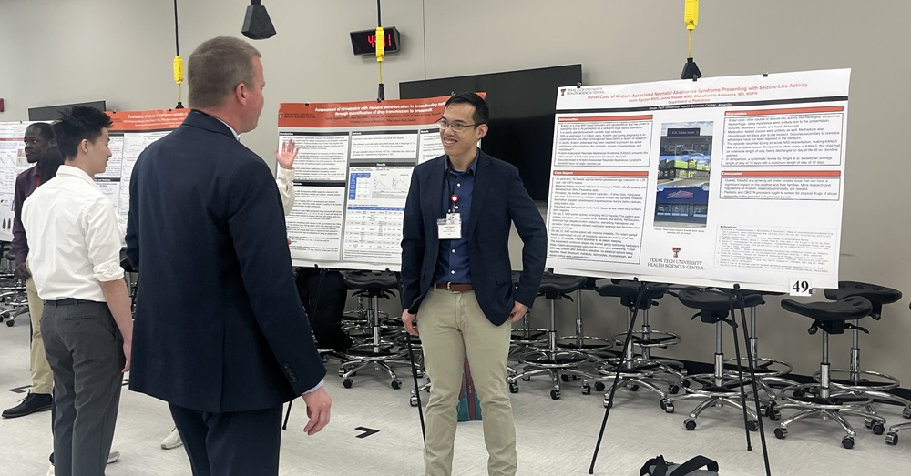 Man standing in front of a research presentation poster, talking to listener