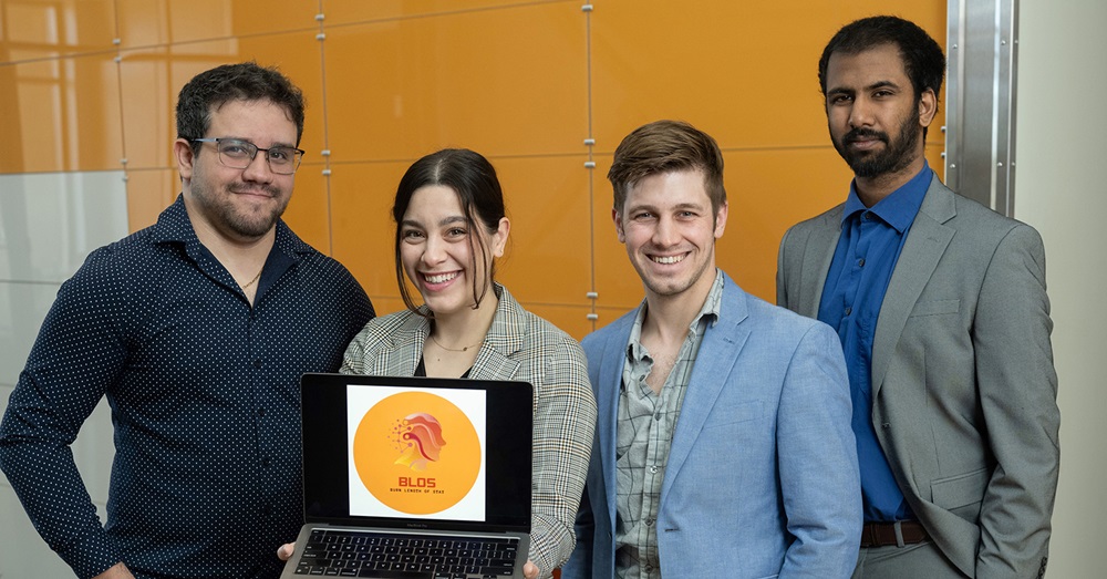 group of four people posing with a laptop