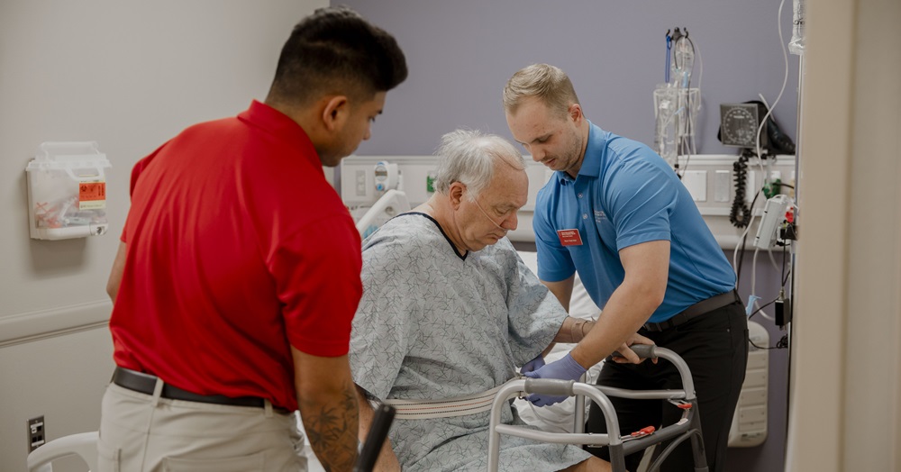 two health care professionals helping an elderly patient in a hospital setting