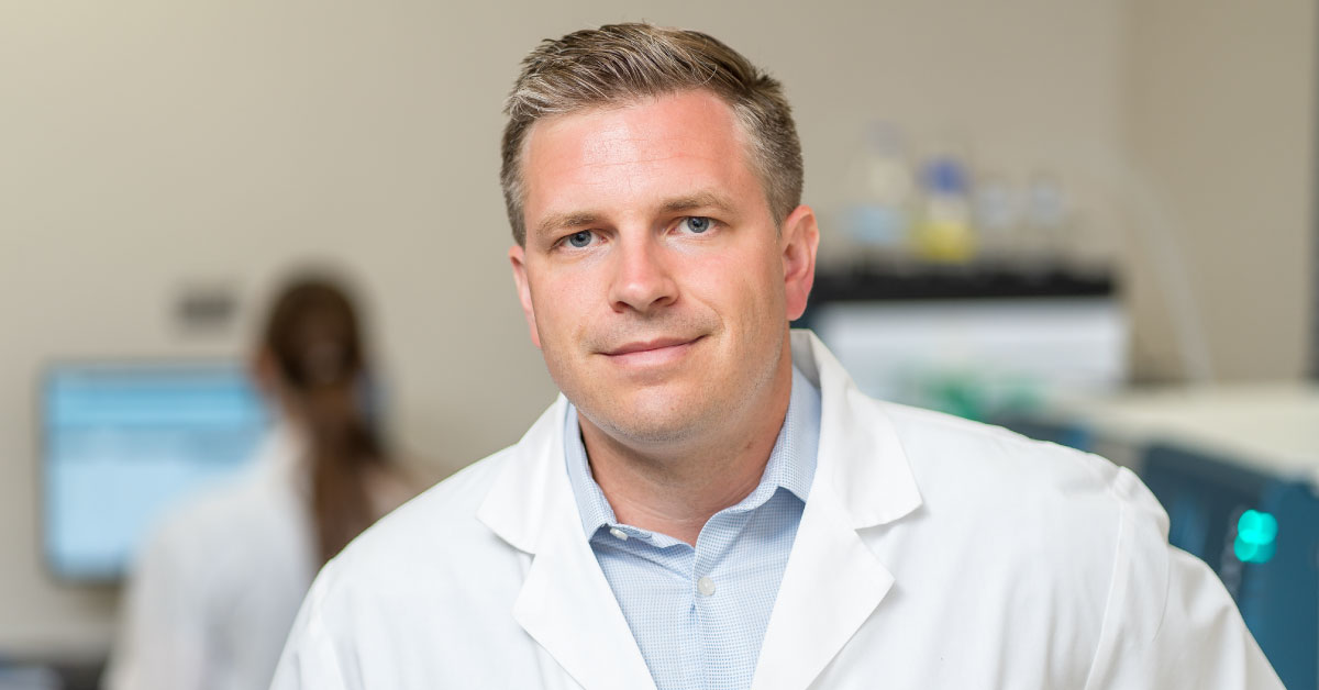 Aric Logsdon wears a white coat in his lab.