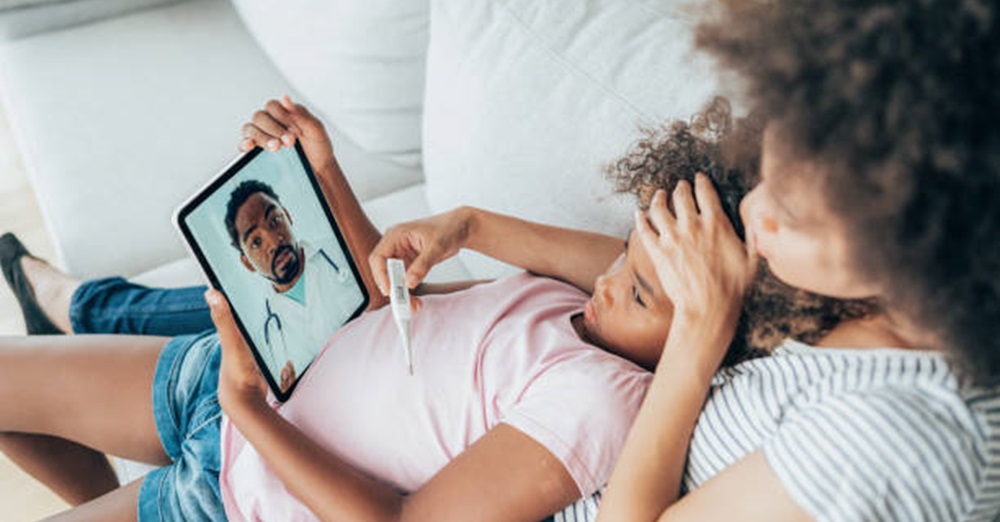 woman with child on a couch talking to a doctor on an ipad for virtual visit