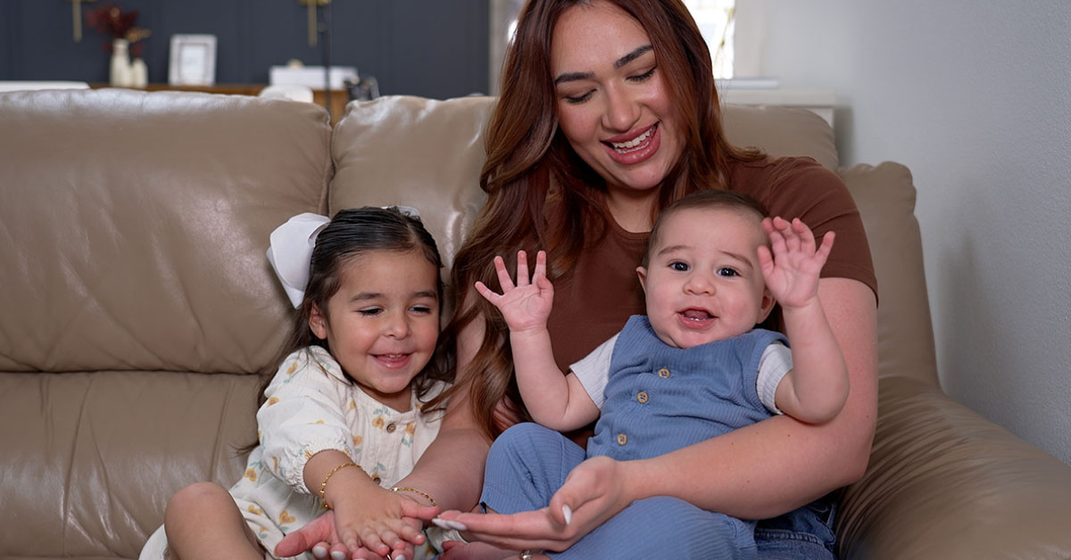 Woman sits on a couch with young girl and baby boy.