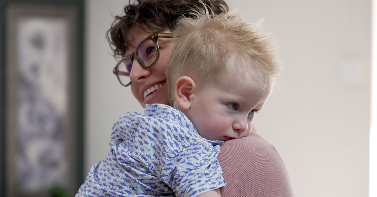 Woman holds a young boy across her chest and shoulder.